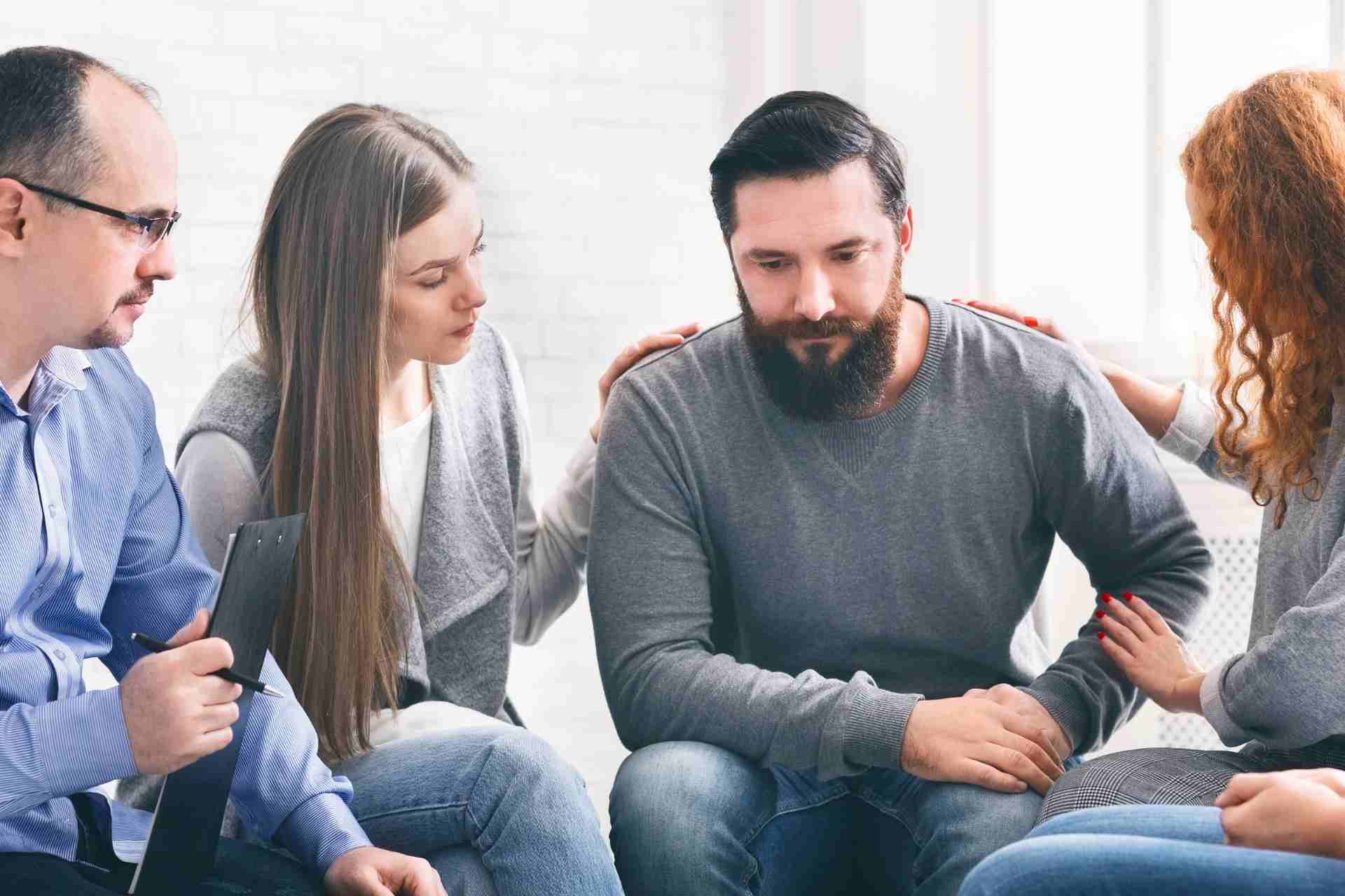 Support group members comforting a man during alcohol addiction recovery