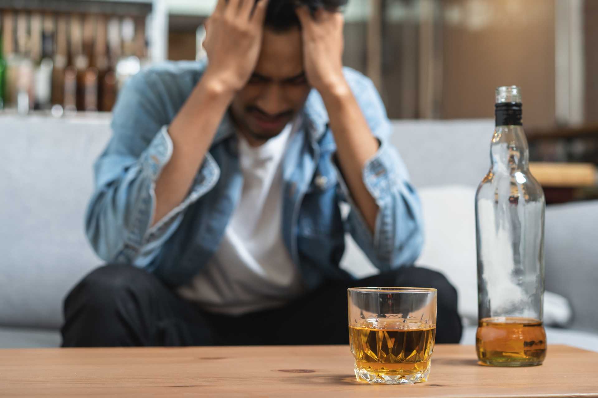 Distressed man sitting behind a glass and bottle of alcohol