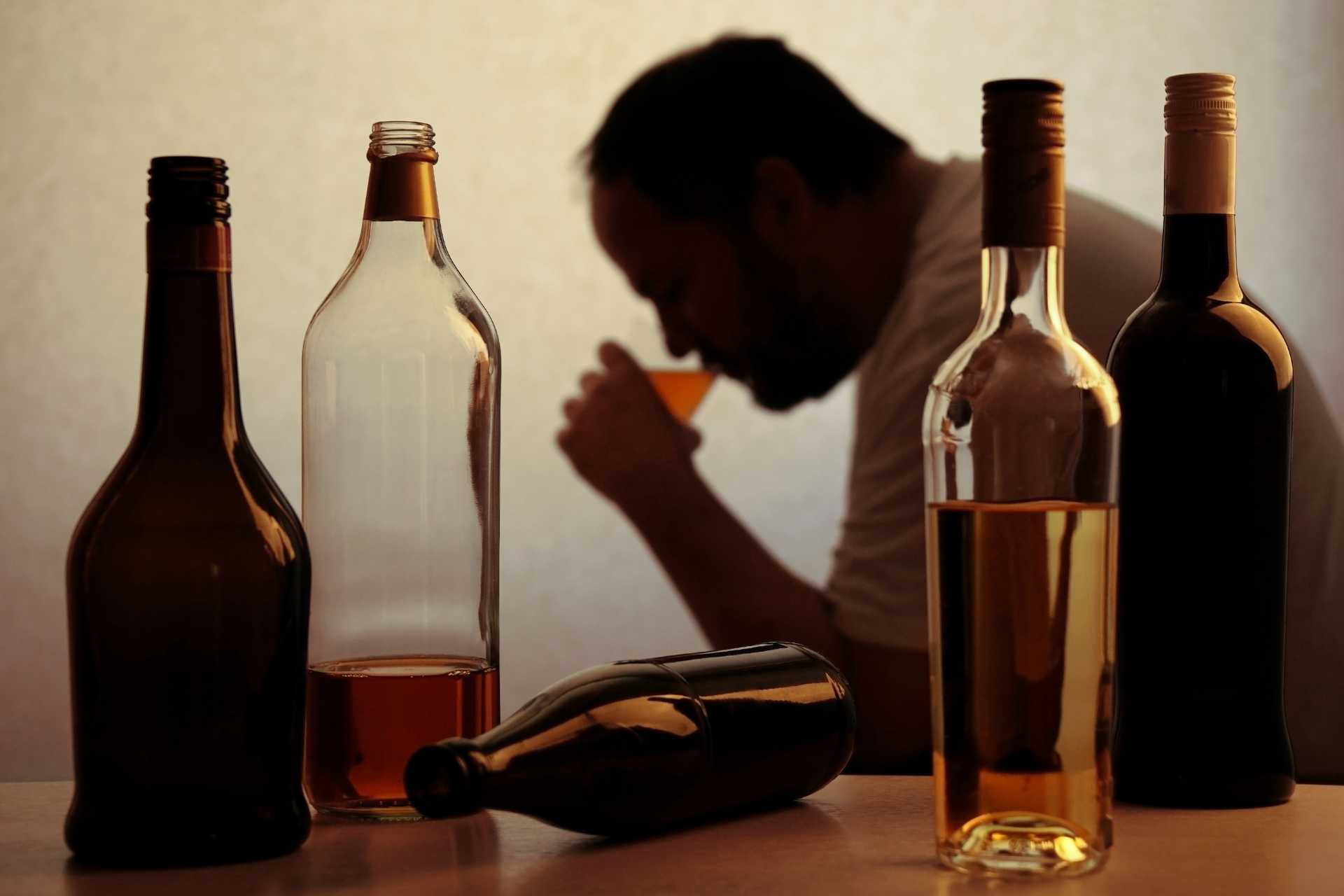 Man drinking alone with several liquor bottles on a table