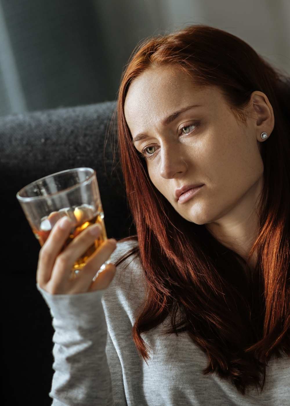 Woman sitting in a chair holding a glass of alcohol and looking distressed