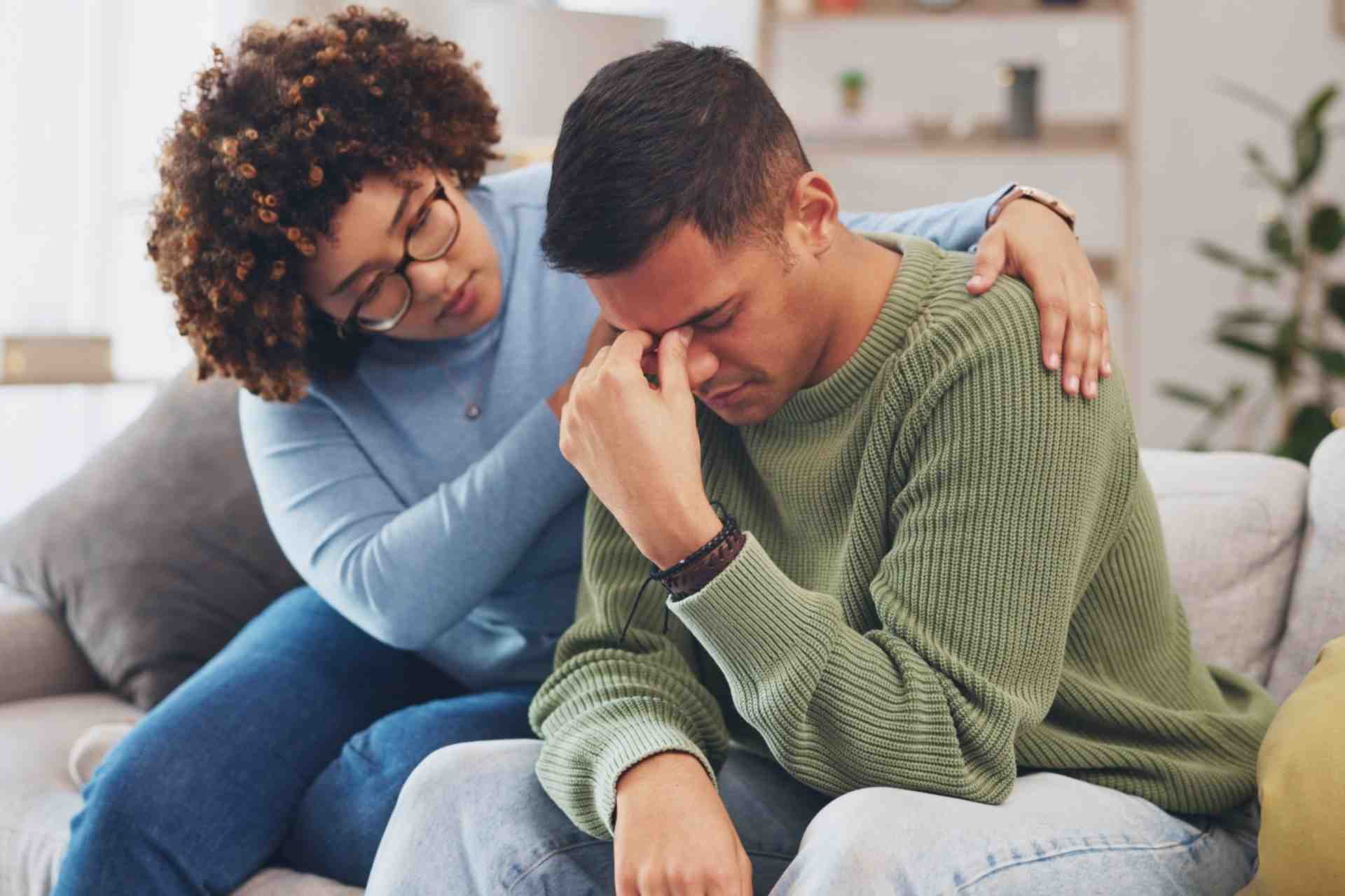Woman comforting a distressed man on a couch during methamphetamine addiction recovery