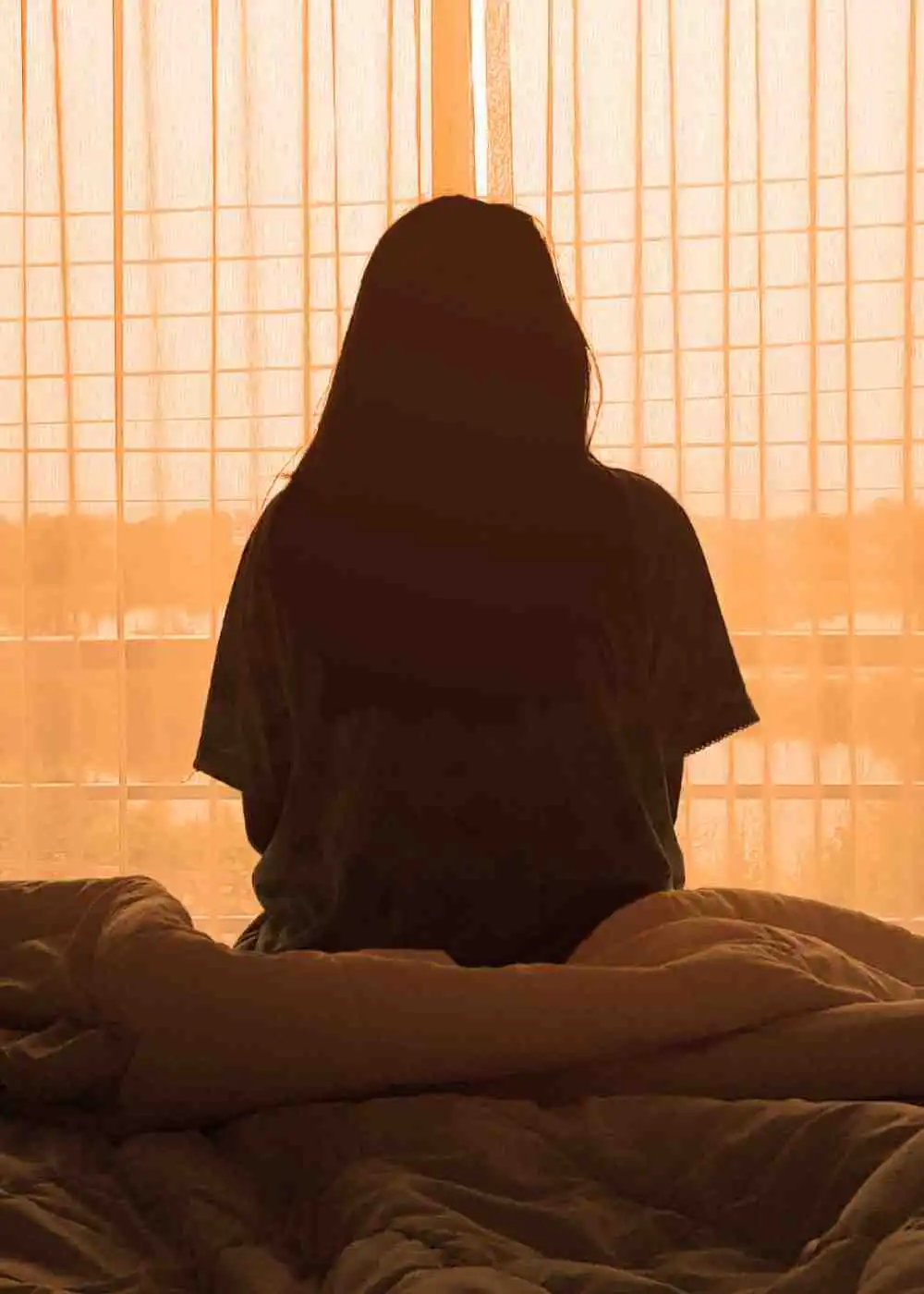 Person sitting alone on a bed in front of a window, representing emotional isolation during methamphetamine withdrawal